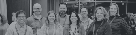 A group of smiling people in front of a conference banner.